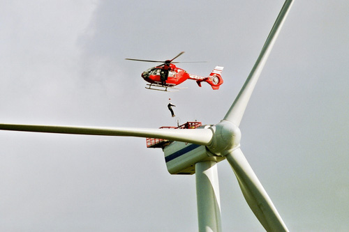 Un hélicoptère hélitreuille des techniciens de maintenance sur une éolienne