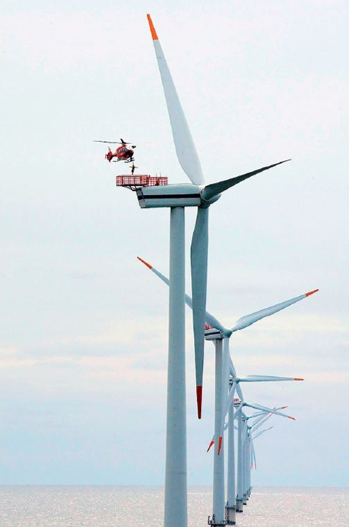 Un hélicoptère hélitreuille des techniciens de maintenance sur une éolienne