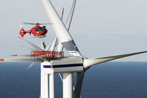 Un hélicoptère hélitreuille des techniciens de maintenance sur une éolienne