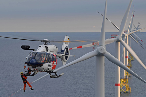 Un hélicoptère hélitreuille des techniciens de maintenance sur une éolienne