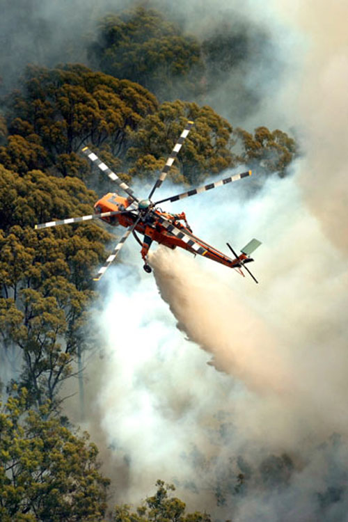 Un hélicoptère S-64 Air Crane largue sa charge d'eau au-dessus des flammes d'un incendie de forêt en montagne