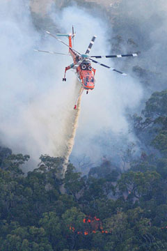 Un hélicoptère S64 AirCrane largue sa charge d'eau au-dessus des flammes d'un incendie de forêt en montagne